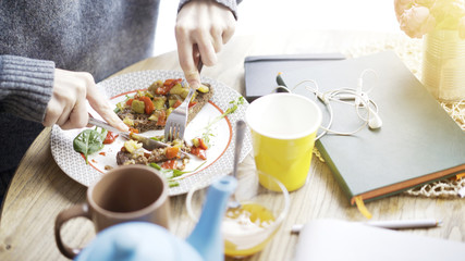 A close up of female hands cutting a tartine of a stew salad on a bread lying on a plate