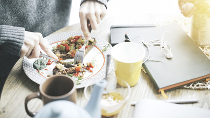 A close up of female hands cutting a tartine of a stew salad on a bread lying on a plate in a cafe