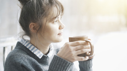 Beautiful woman wearing a gray sweater is enjoying her tea in a cafe and daydreaming. Portrait shot