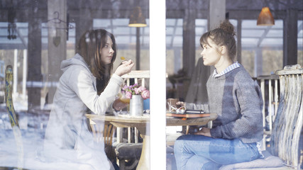 Fototapeta na wymiar Two casual cute female friends smiling having a light talk met in a cafe to talk and eat dessert and drink tea
