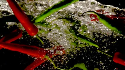 Fresh red and green peppers are falling into water with splash on black background close-up slow motion - Powered by Adobe