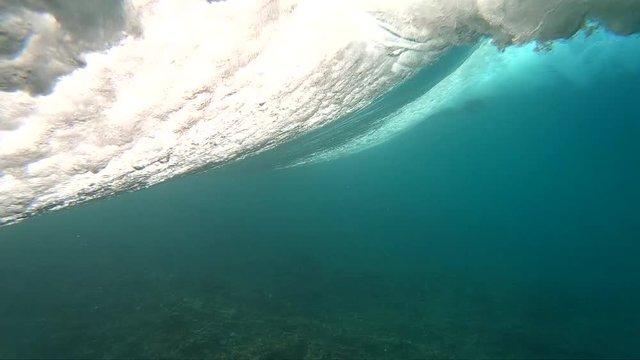 Underwater view of surfing wave spinning vortex with surfer paddling