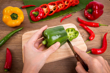 woman hands cutting green bell pepper on wood background with wooden board