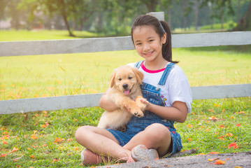 Young asian girl holding a little golden retriever dog in park