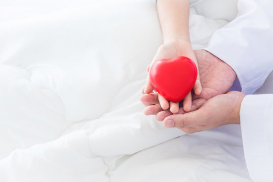 Hands Of Child And Male Doctor Holding Red Heart Ball Together