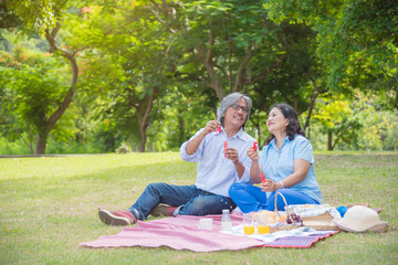 Happy asian retired couple blowing bubbles in park.