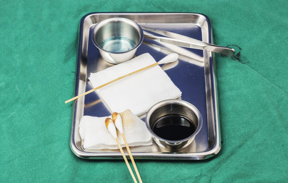 Dressing set on green cloth. septic solution on silver cup,cotton butt,gauze, forceps in silver tray on green background.