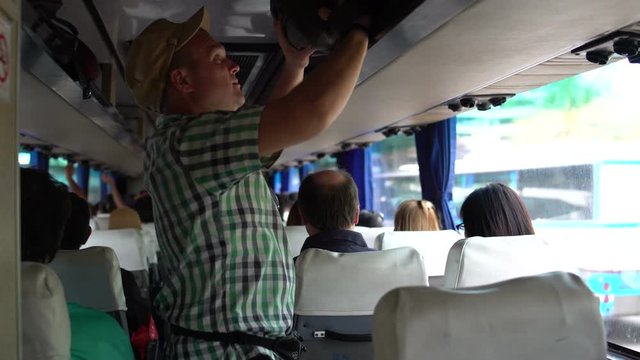 A man walks through the cabin of the bus, removes the bag on the luggage rack and sits down