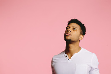Close up portrait of a young man looking up and left with interest, , isolated on pink studio background