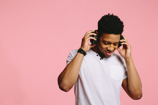 Man listening on headphones, enjoying and looking down, isolated on pink background