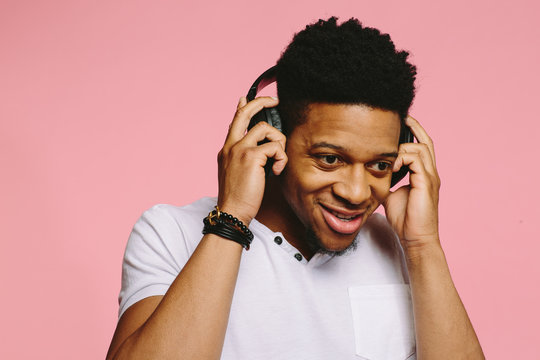 Portrait of a smiling guy in white shirt listening to music on pink background