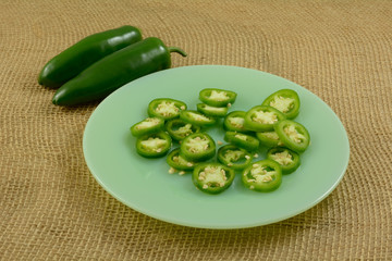 Jalapeno pepper ring slices on green plate with two whole raw jalapeno peppers on side