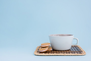Big cup of coffee and sandwich cookies on blue background