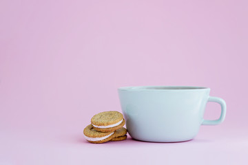 Big cup of coffee and sandwich cookies on pink background