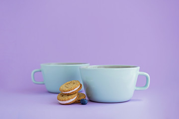 Two big cups of coffee and sandwich cookies on violet background