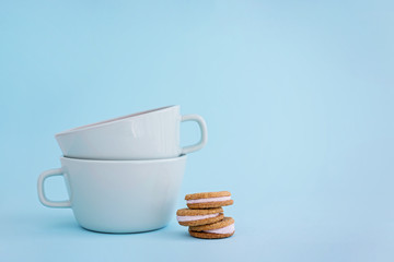 Two big cups of coffee and sandwich cookies on blue background