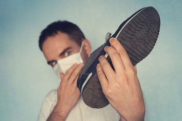 Man with mask is holding dirty stinky shoe - unpleasant smell concept. Dirty smelly sneakers.