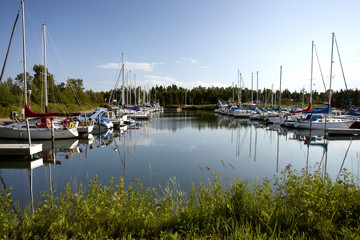 Fototapeta na wymiar View of a marina on Lake Superior full of boats and sailboats. Clear blue sky and calm water reflecting the scene.