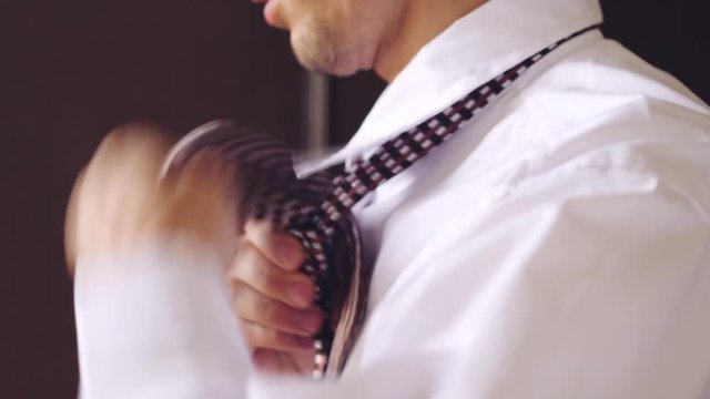 Profile of a young man in white shirt tying a tie. 3840x2160