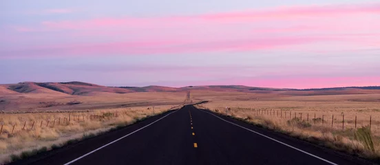 Selbstklebende Fototapete Candy Pink Flat Two Lane Blacktop Highway führt in den rosa Sonnenuntergang