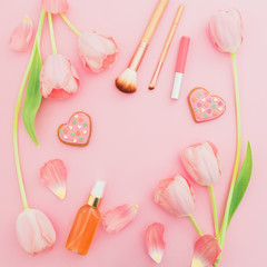 Frame with pink flowers, cosmetics and cookies on pink pastel background. Flat lay, top view with copy space