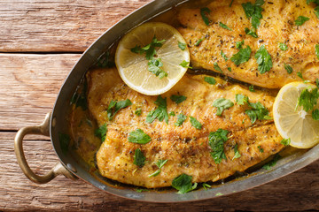 Baked trout fish with garlic lemon butter sauce, parsley closeup in a copper pan on a table. horizontal top view