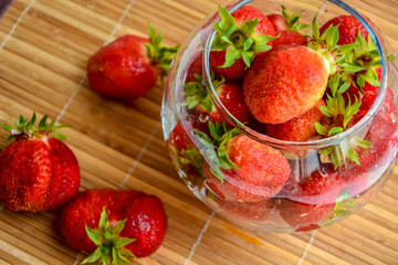 Red ripe strawberry with green leaves in a transparent glass vase in the shape of a ball on a wooden background