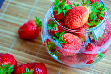 Red ripe strawberry with green leaves in a transparent glass vase in the shape of a ball on a wooden background