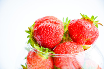 Red ripe strawberry with green leaves in a transparent vase in the shape of a ball on a light background
