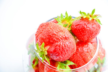 Red ripe strawberry with green leaves in a transparent vase in the shape of a ball on a light background