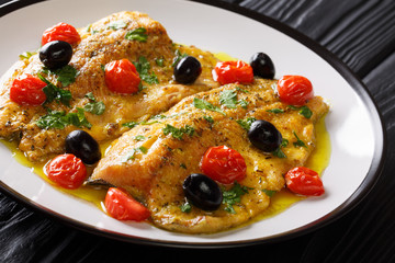 Italian food: fried trout fillets with garlic lemon butter sauce, tomatoes, parsley and olives close-up on a plate. horizontal