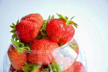 Red ripe strawberry with green leaves in a transparent vase in the shape of a ball on a light background