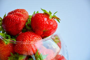 Red ripe strawberry with green leaves in a transparent vase in the shape of a ball on a light background