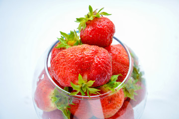 Red ripe strawberry with green leaves in a transparent vase in the shape of a ball on a light background