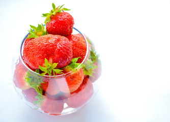 Red ripe strawberry with green leaves in a transparent vase in the shape of a ball on a light background