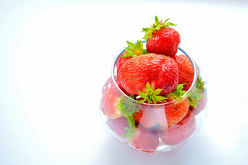 Red ripe strawberry with green leaves in a transparent vase in the shape of a ball on a light background