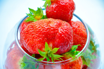 Red ripe strawberry with green leaves in a transparent vase in the shape of a ball on a light background
