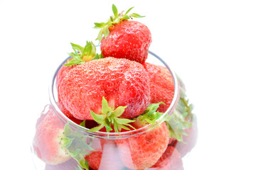Red ripe strawberry with green leaves in a transparent vase in the shape of a ball on a light background