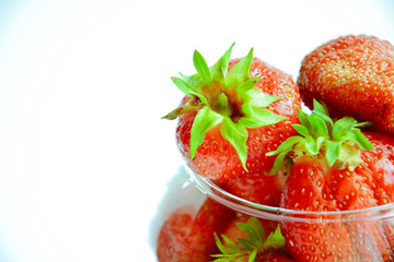 Red ripe strawberry with green leaves in a transparent vase in the shape of a ball on a light background