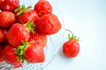 Red ripe strawberry with green leaves in a transparent glass plate on a light background
