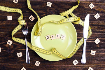 Diet concept represented by plate, cutlery and yellow measuring tape on wooden table