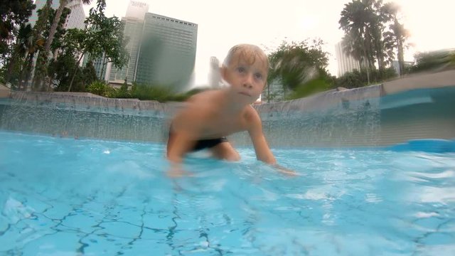 Slowmotion shot of a little boy having fun in a pool in the park around the Petronas towers Kulala-Lumpur, Malaysia