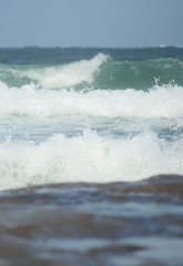 The foam of waves breaking over a brown rock. The water is pale aqua, becoming darker towards the horizon.