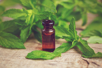 Natural Mint essential oil in a glass bottle with fresh min leaves on a wooden background.