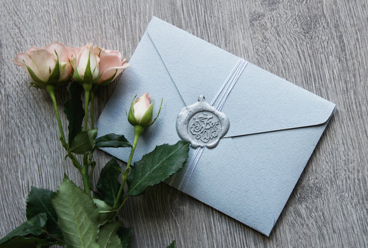 Flat lay stylish mockup photo with envelope with seal wax and roses bouquet flowers on the light wooden background. Feminine photo for blog and website.