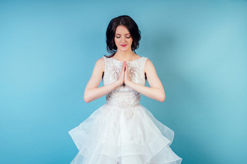 Fototapeta na wymiar young and beautiful calm woman bride with makeup in chic white wedding dress practicing yoga and meditating in studio on a blue background .