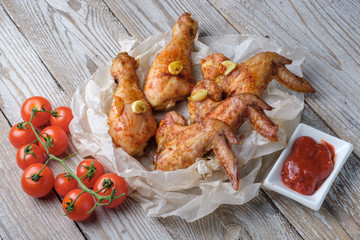Baked chicken legs and wings lie on the table. Nearby are cherry tomatoes, celery, parsley and spices.