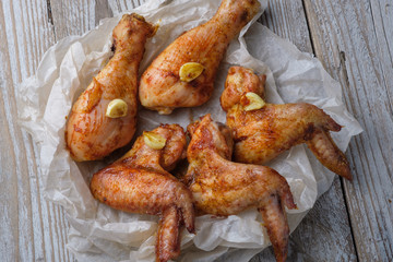 Baked chicken legs and wings lie on the table. Nearby are cherry tomatoes, celery, parsley and spices.