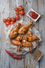 Baked chicken legs and wings lie on the table. Nearby are cherry tomatoes, celery, parsley and spices.
