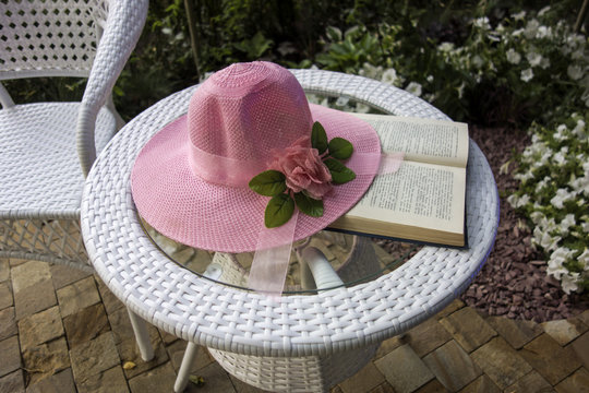 White country wicker furniture, pink hat on the table and a book